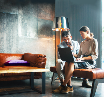 Two colleagues sitting on a bench trying to work out a problem on a laptop.